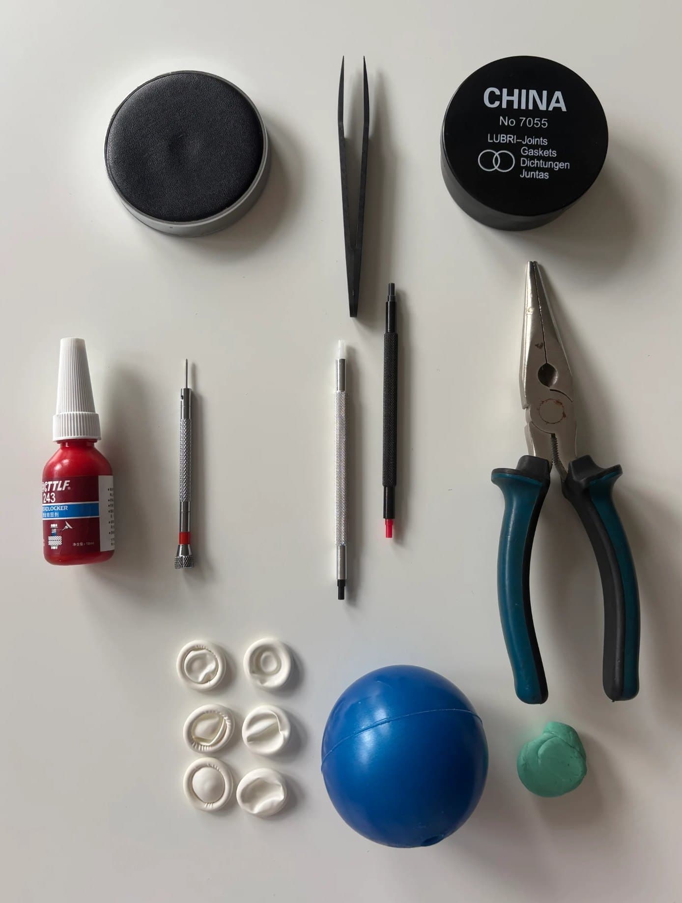 The ten Essentials tools laid out - movement cushion, plastic tweezers, silicone greaser, threadlocker, screwdriver, hand attachers, pliers, finger cots, watchmaking ball and putty