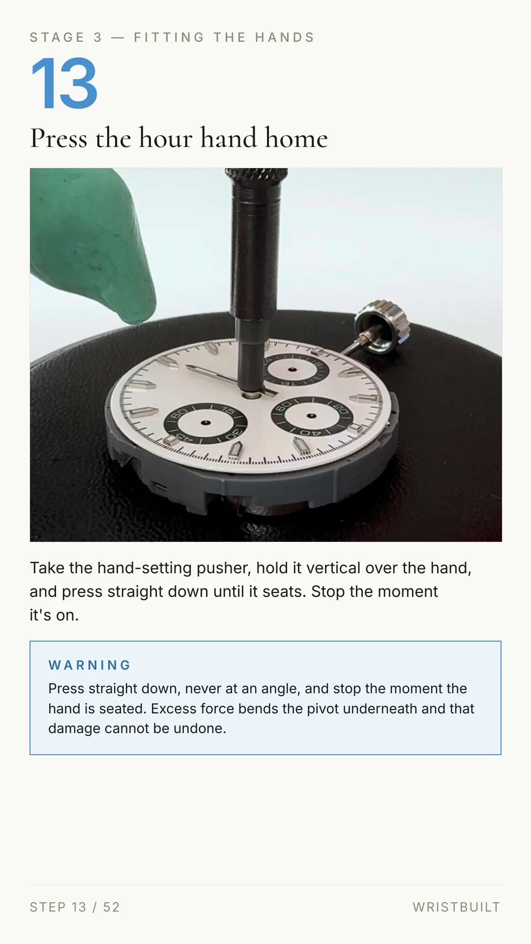 STAGE 3 — FITTING THE HANDS 13 Press the hour hand home Take the hand-setting pusher, hold it vertical over the hand, and press straight down until it seats. Stop the moment it's on. WARNING Press straight down, never at an angle, and stop the moment the hand is seated. Excess force bends the pivot underneath and that damage cannot be undone. STEP 13 / 52 WRISTBUILT